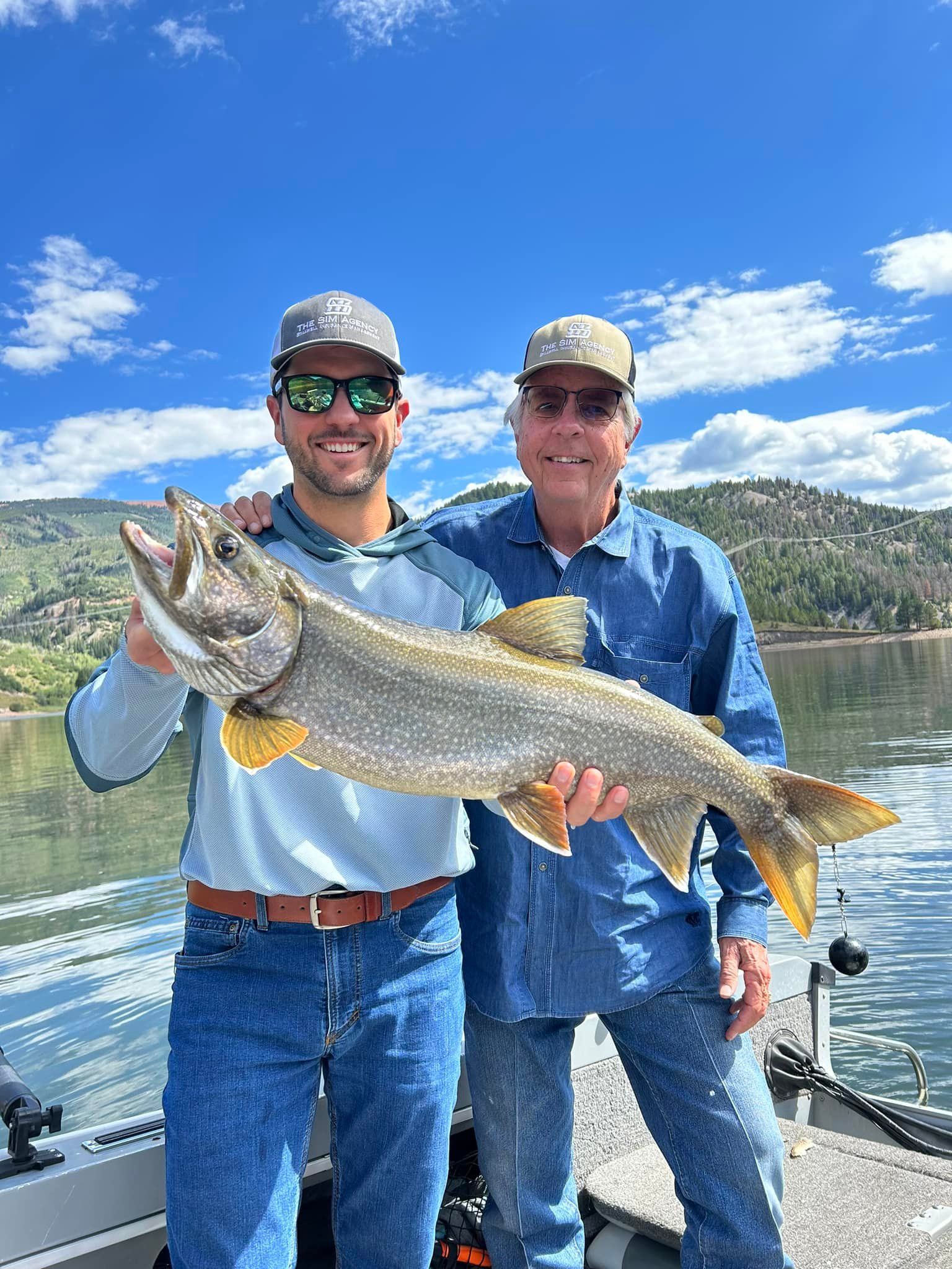 Two men are standing on a boat holding a large fish.