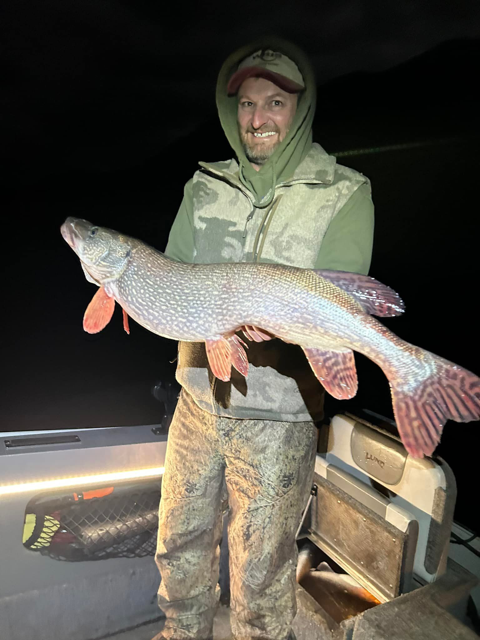 A man is standing on a boat holding a large fish.
