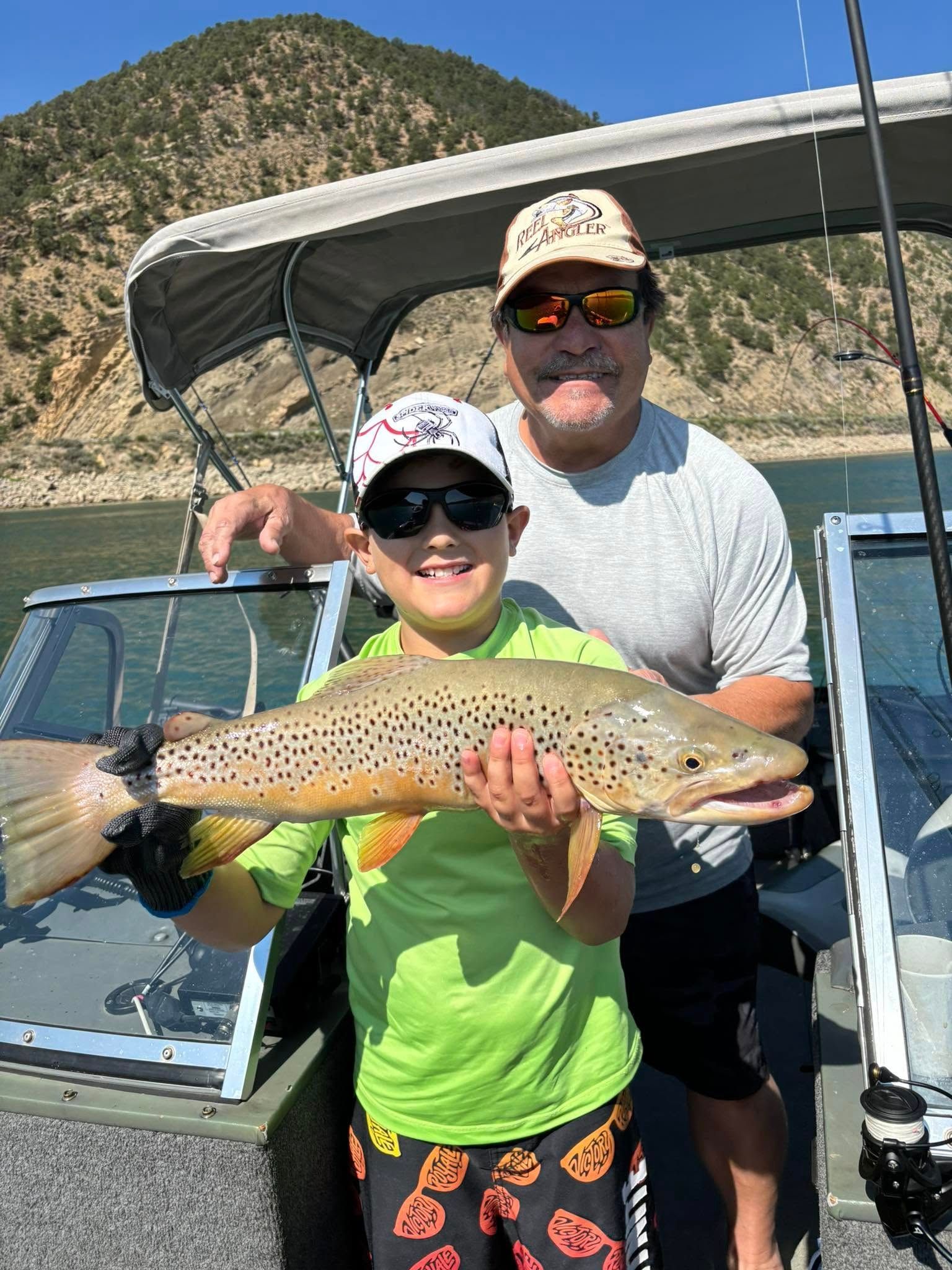 A man and a boy are holding a brown trout on a boat.