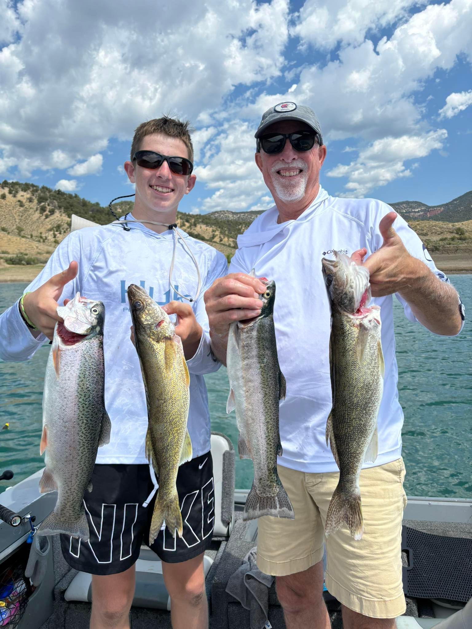 A man and a boy are holding fish on a boat and giving a thumbs up.