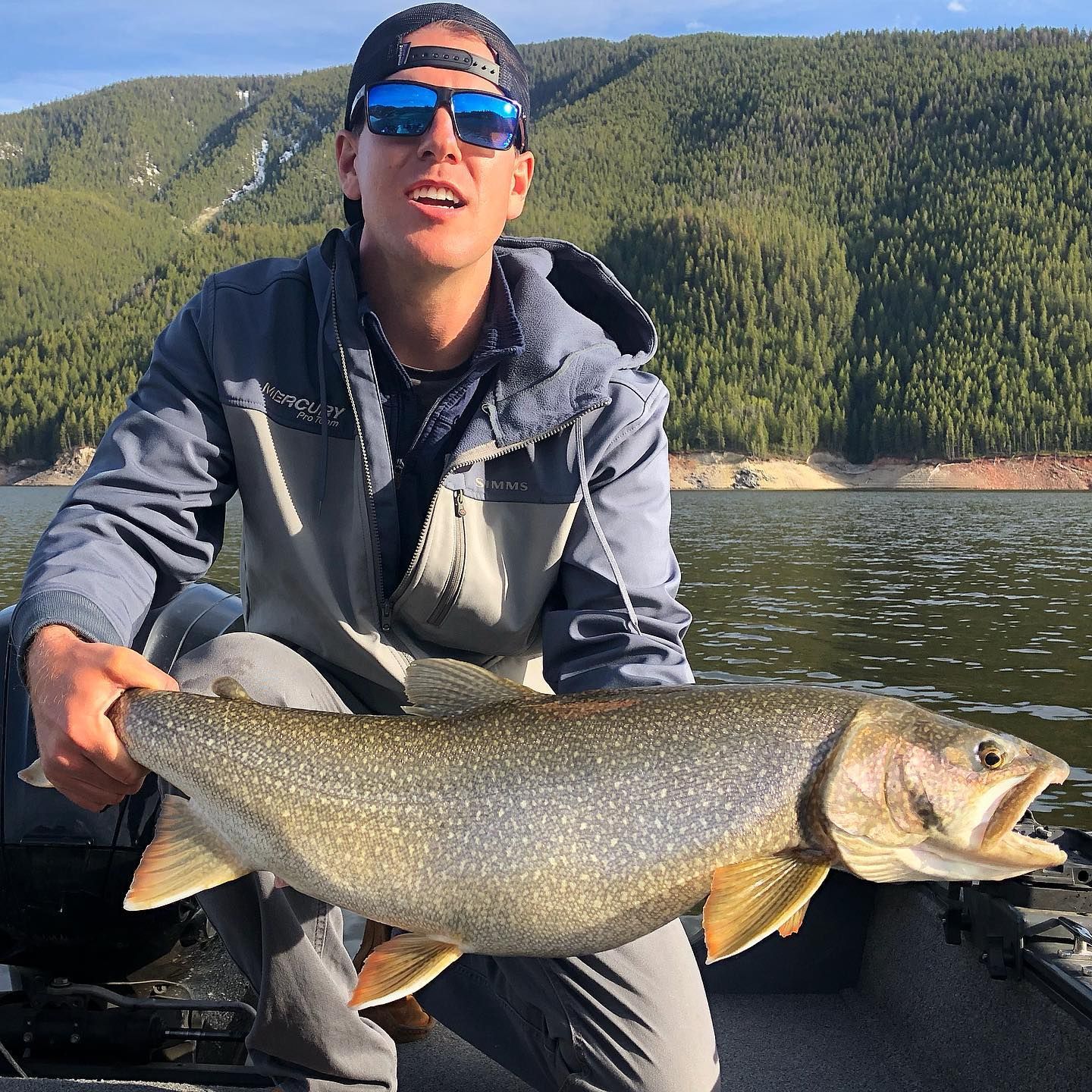 A man is sitting on a boat holding a large fish.