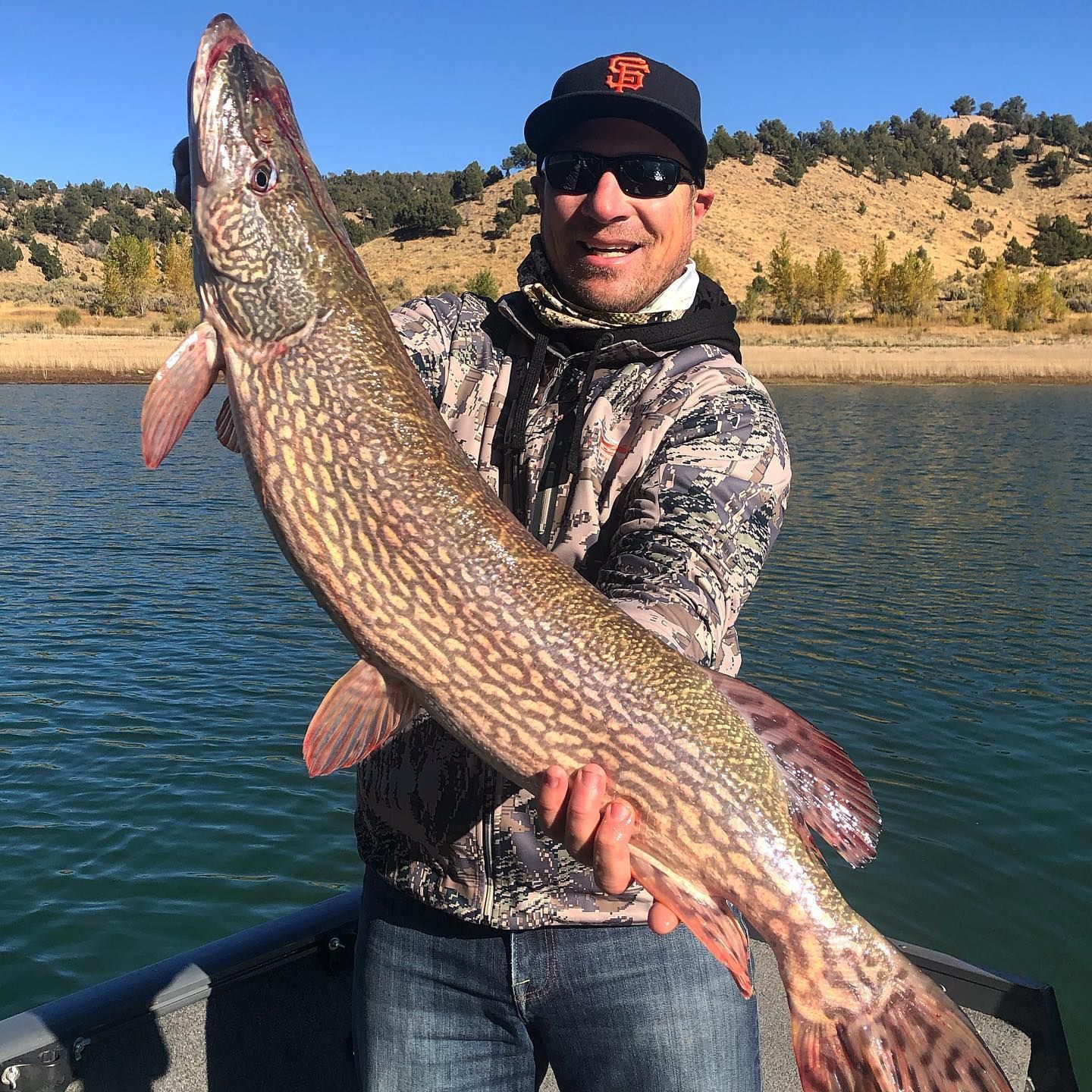 A man is holding a large fish in front of a lake.