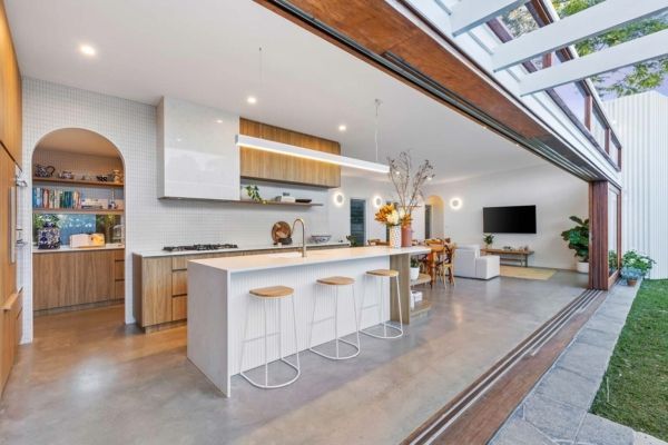 Open-concept kitchen with white island, wood cabinets, and large doors opening to a yard — PK Kitchen Design in West Ipswich, QLD