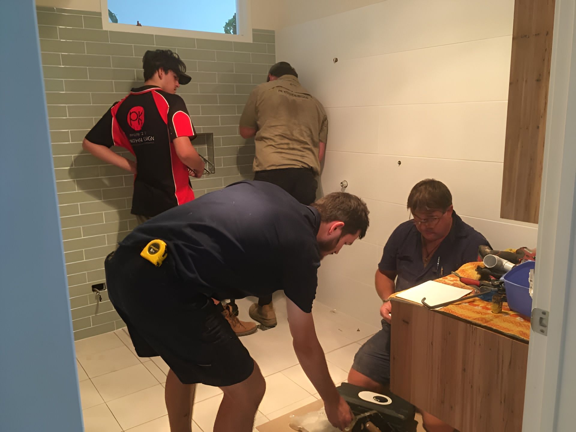 Four Men Working in a Bathroom, Installing a Cabinet and Tiles — PK Kitchen Design in West Ipswich, QLD
