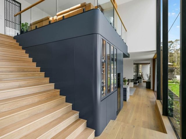 Wooden staircase next to a dark blue wall with a glass-walled structure; leading to a light-filled corridor — PK Kitchen Design in West Ipswich, QLD