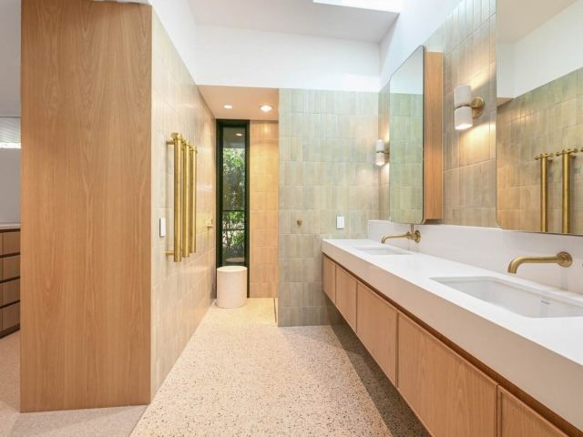 Bathroom with light wood cabinets, white sinks, gold fixtures, and textured walls and floor — PK Kitchen Design in West Ipswich, QLD