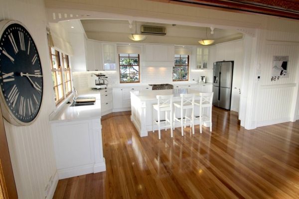 Bright white kitchen with a wooden floor, island with stools, and large wall clock — PK Kitchen Design in West Ipswich, QLD