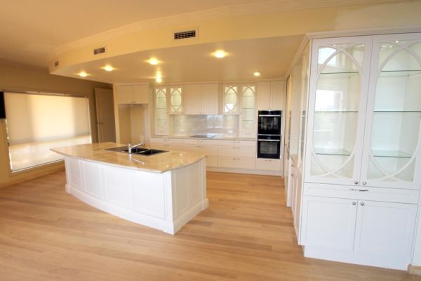 Spacious white kitchen with light wood floors, an island, and built-in appliances — PK Kitchen Design in West Ipswich, QLD