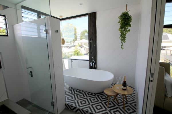 Modern bathroom with white tub, geometric floor tiles, glass shower, and hanging plant — PK Kitchen Design in West Ipswich, QLD