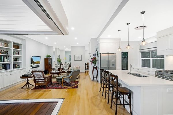 Open-plan living space with kitchen, lounge, and dining areas. Light wood floors, white cabinetry, and stainless steel appliances — PK Kitchen Design in West Ipswich, QLD