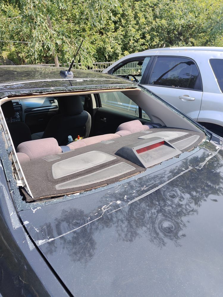 A black car with a broken windshield is parked in a parking lot.
