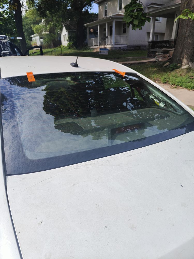 A white car with a broken windshield is parked in front of a house.