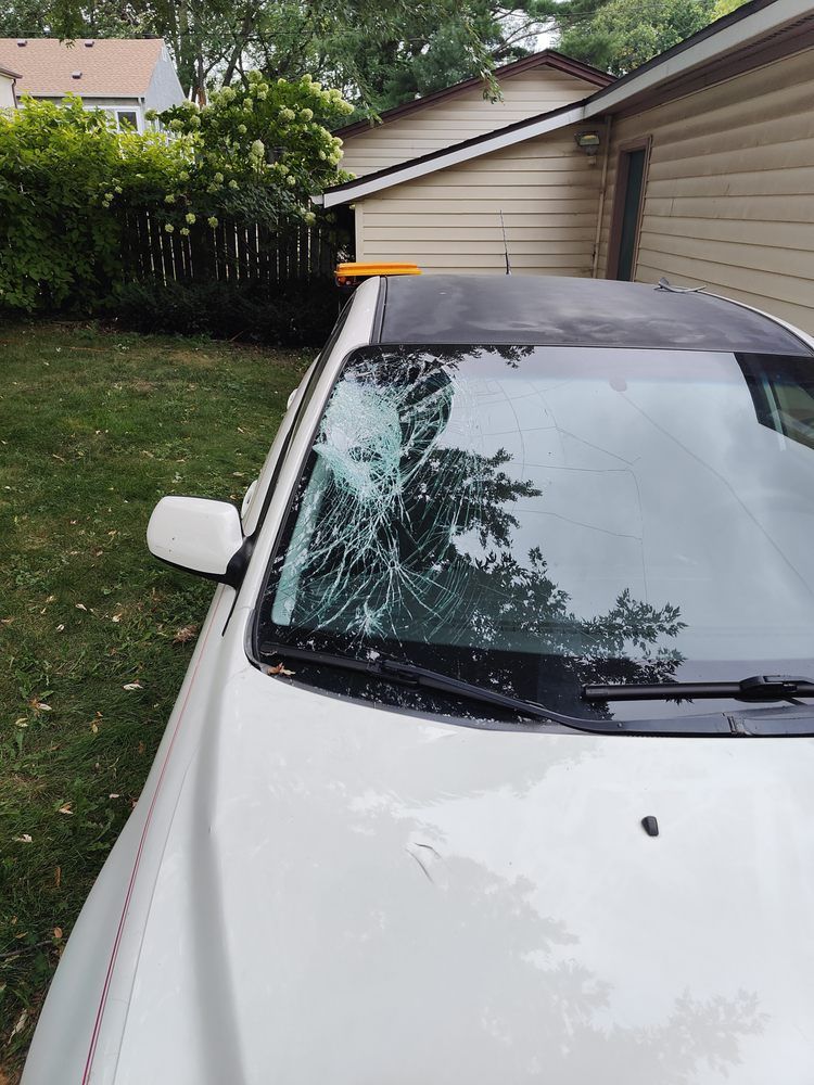 A white car with a broken windshield is parked in front of a house.