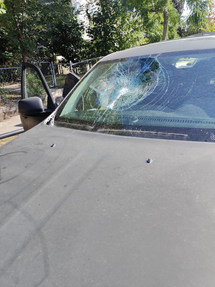 A black car with a broken windshield is parked on the side of the road.