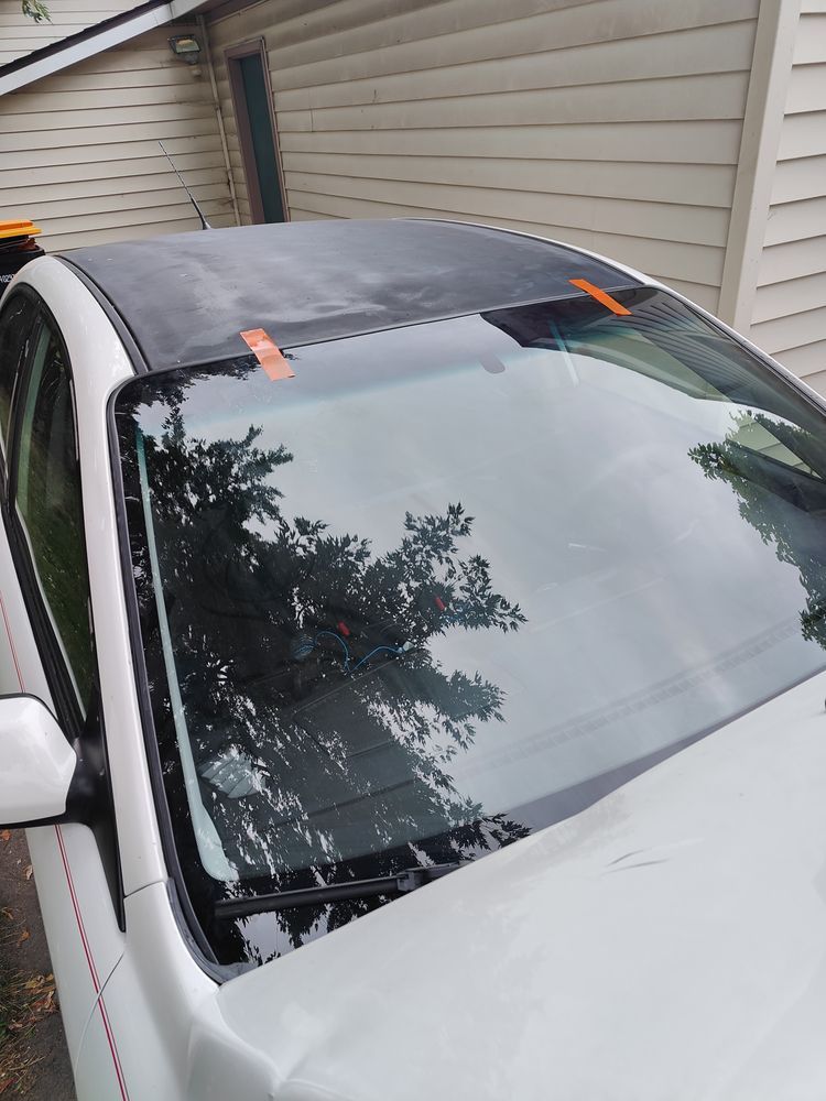 A white car with a black roof is parked in front of a house.