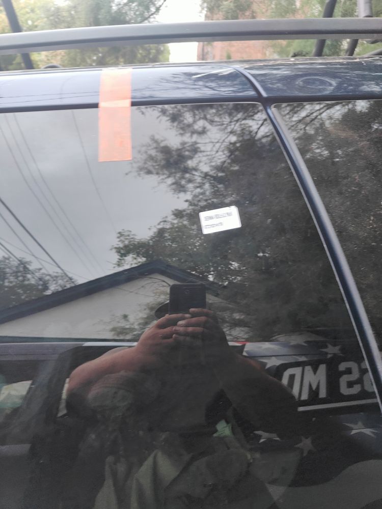 A person is taking a picture of their reflection in a car window.