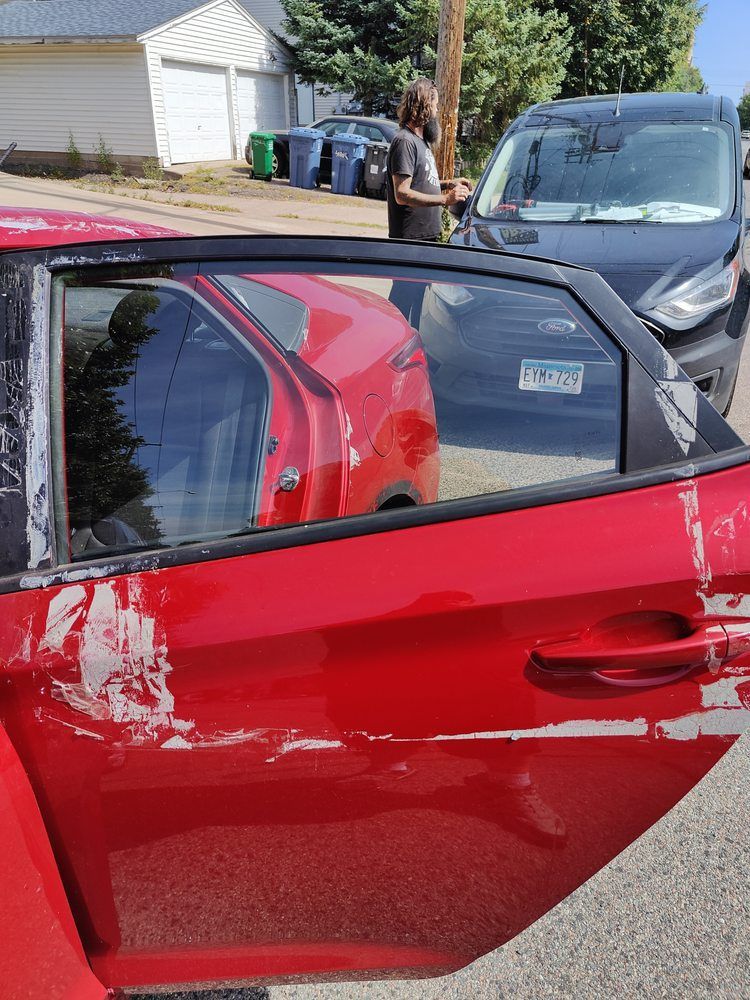 A red car with a damaged door is parked on the side of the road.