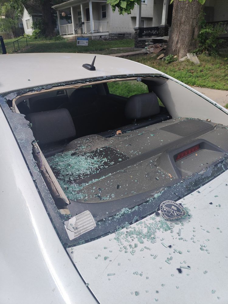 A car with a broken windshield is parked in front of a house