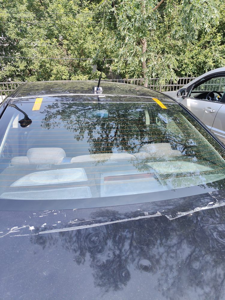 A black car is parked in a parking lot with trees in the background.