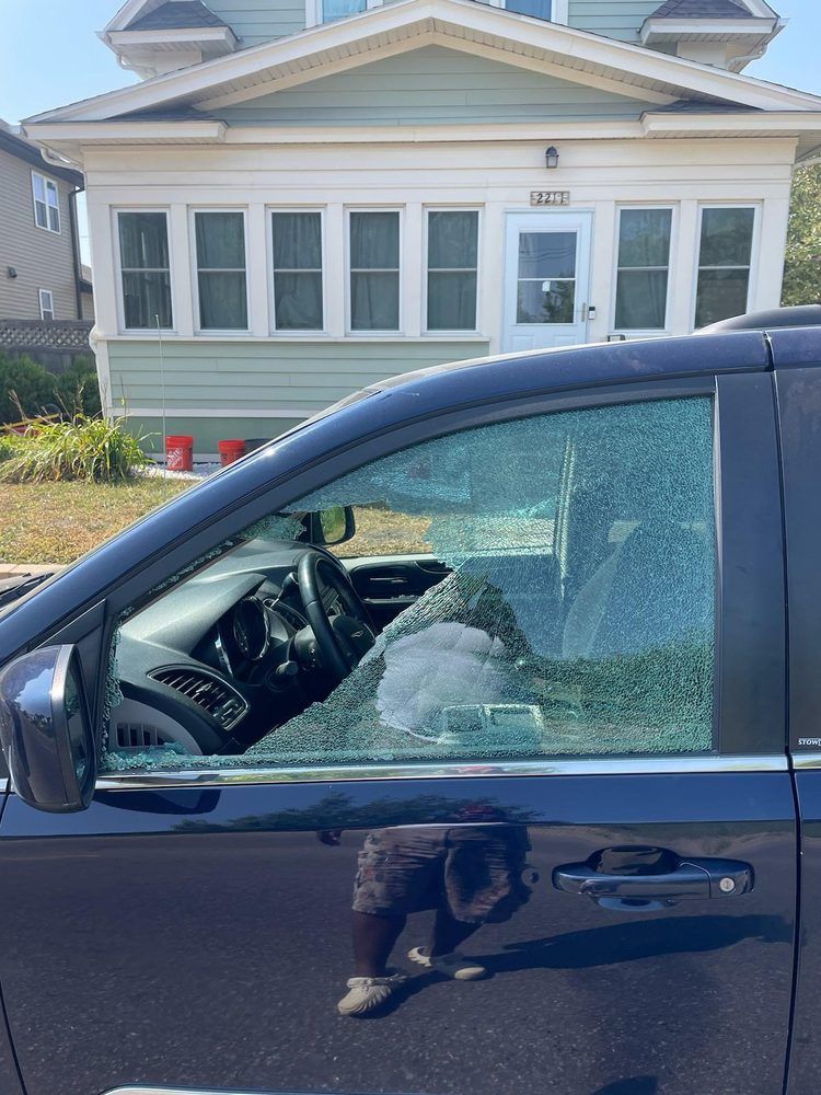 A car with a broken windshield is parked in front of a house.