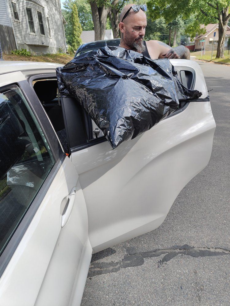 A man is carrying a large black bag out of the back of a car.