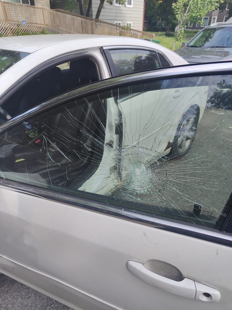A white car with a broken windshield is parked in a driveway.