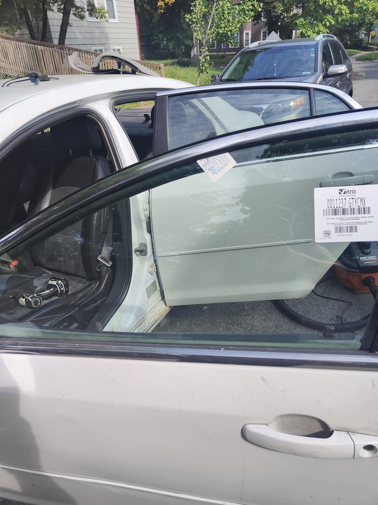 A white car with a tag on the door is parked in front of a house.