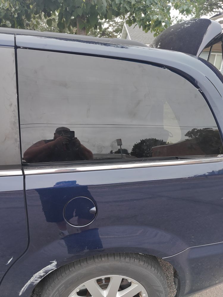 A blue car with a reflection of a person in the window.