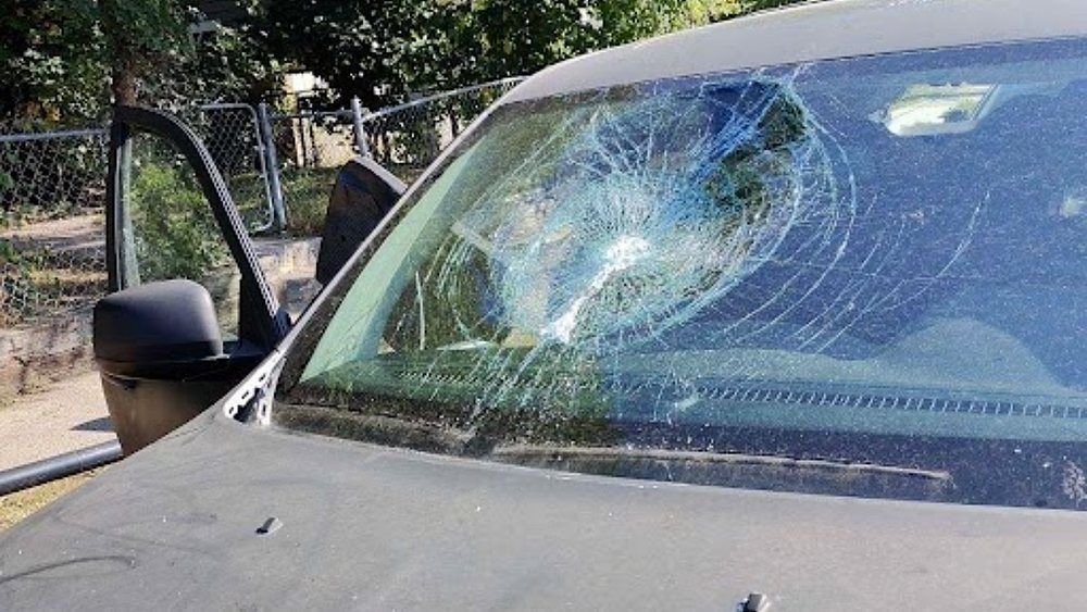 A car with a broken windshield is parked on the side of the road.