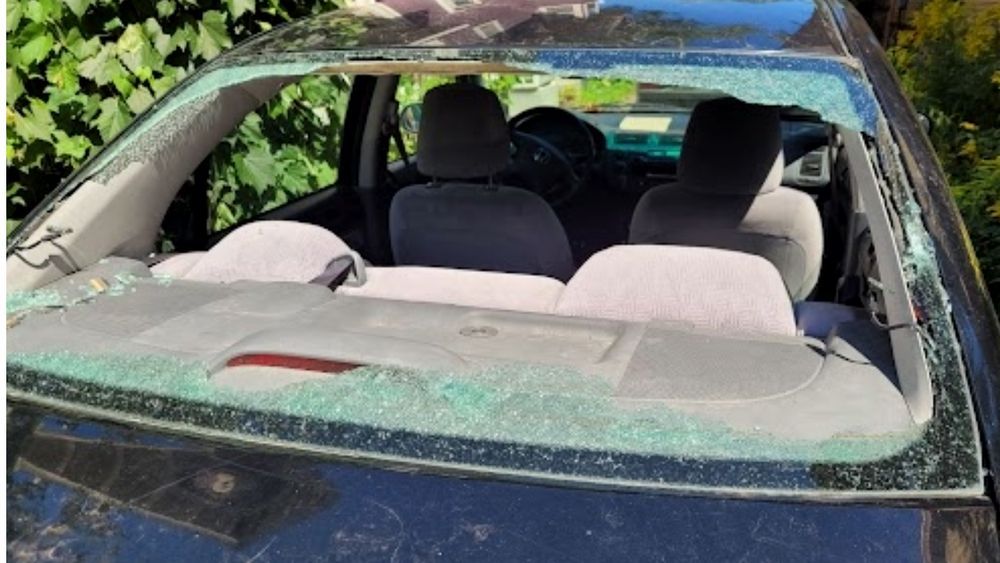 A car with a broken windshield is parked in a driveway.