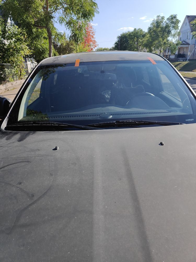 A black car with a broken windshield is parked on the side of the road.
