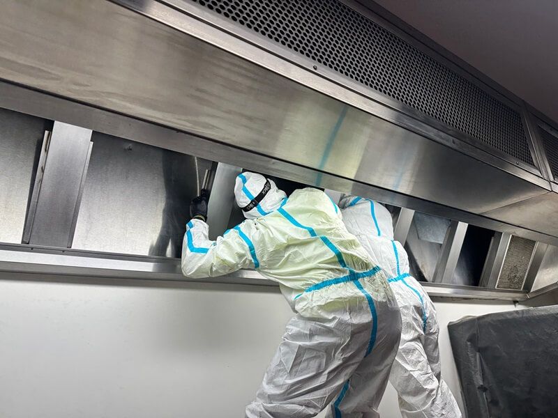 Two people in hazmat suits cleaning a commercial kitchen hood.