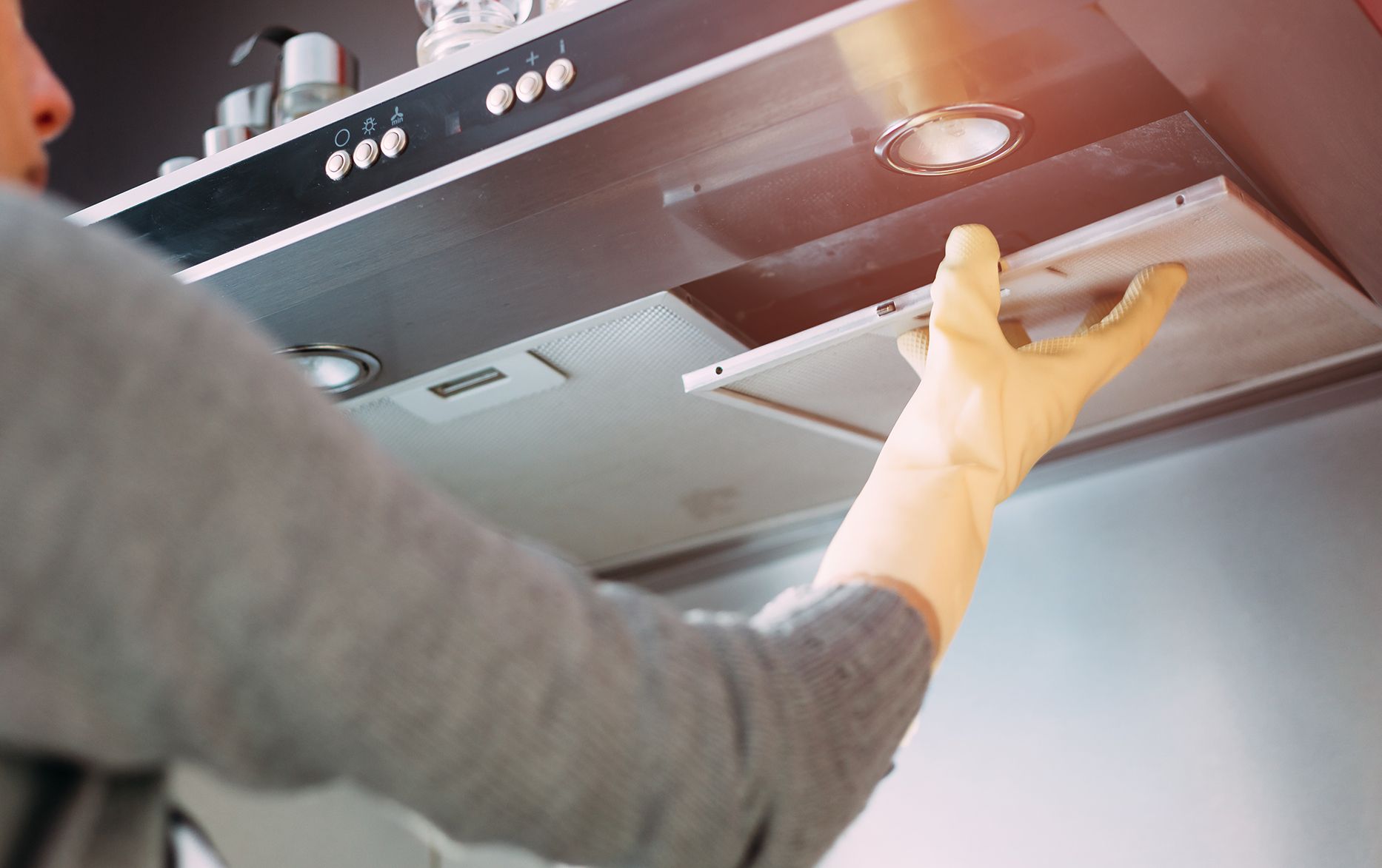 Person in grey shirt and gloves removing a filter from a stainless steel range hood.