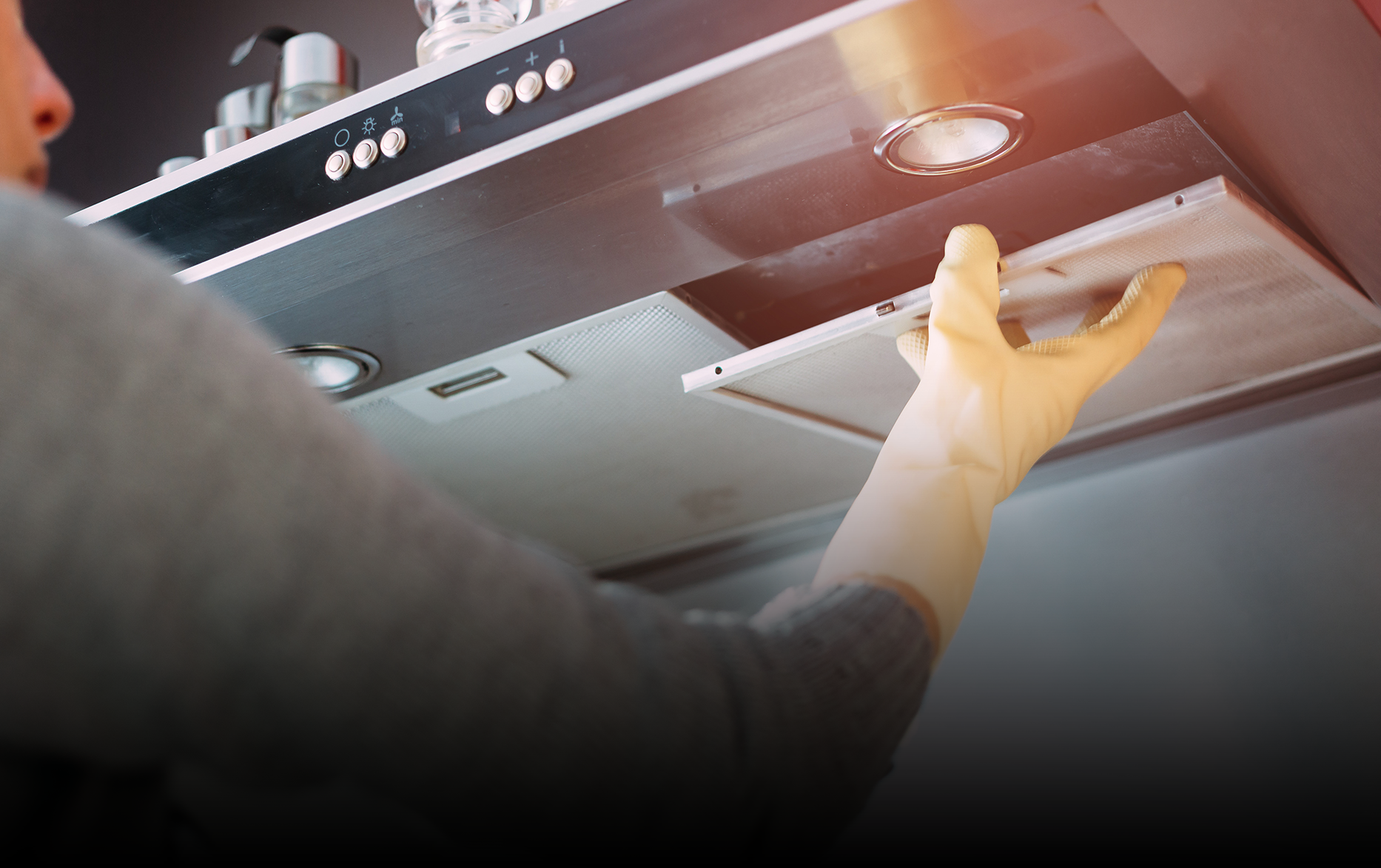 Person wearing a glove removing a dirty range hood filter in a kitchen.