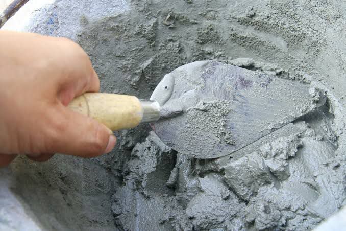 Uma pessoa está misturando concreto em um balde com uma espátula.