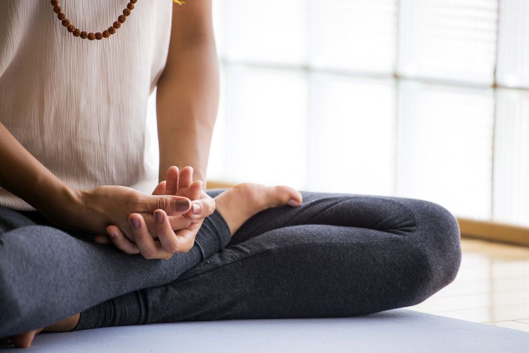 Woman meditating on a mat in sunlight, eyes closed, wearing a green top and pink pants.