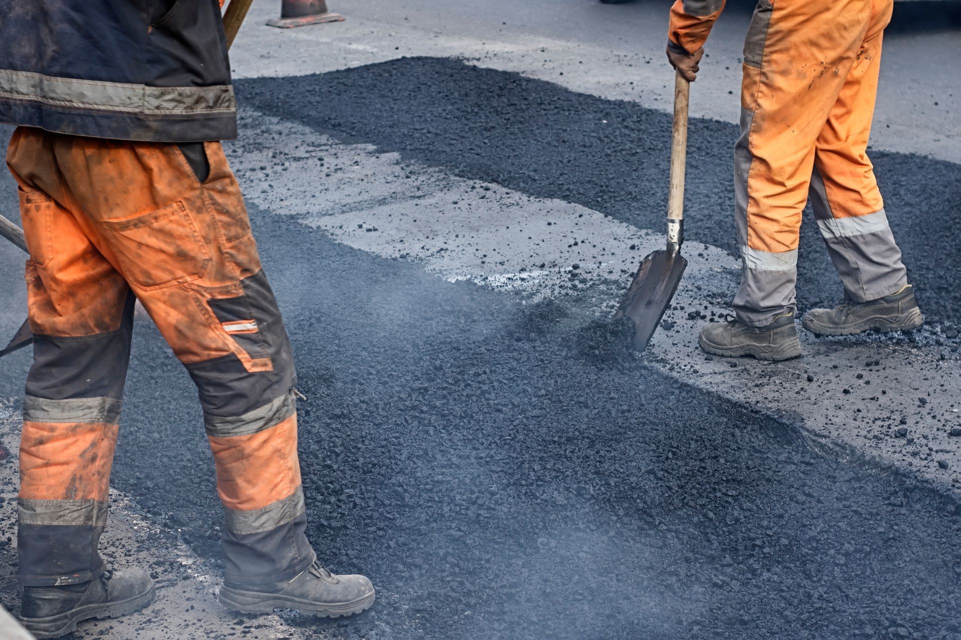 Road workers in orange workwear shoveling asphalt onto a road.