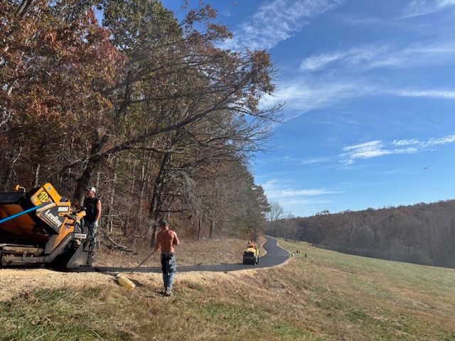 Men paving a path near a wooded area. Blue sky, fall colors. Asphalt machine.