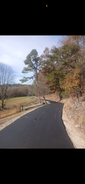 Asphalt road winding through a wooded area with trees displaying autumn colors.