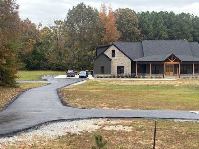 Paved driveway leads to a modern home with stone and wood accents; cars parked in front.