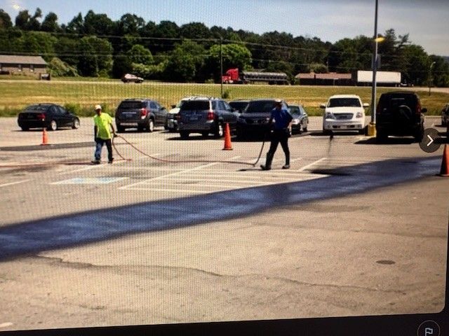 Applying black sealant to a crack in pavement with a roller and applicator.