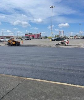 Newly paved asphalt surface with construction equipment in a parking lot on a sunny day.