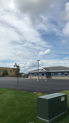 Building with blue siding, dark asphalt parking lot, blue sky with clouds.