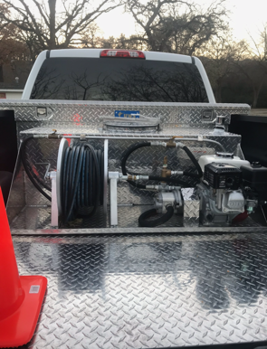A pickup truck bed with a diamond-plated tool box and equipment, including a hose reel and engine.