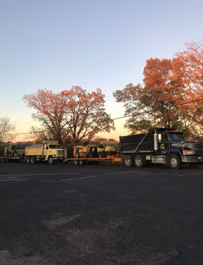 Trucks hauling heavy equipment in an outdoor setting with trees and a dusky sky.