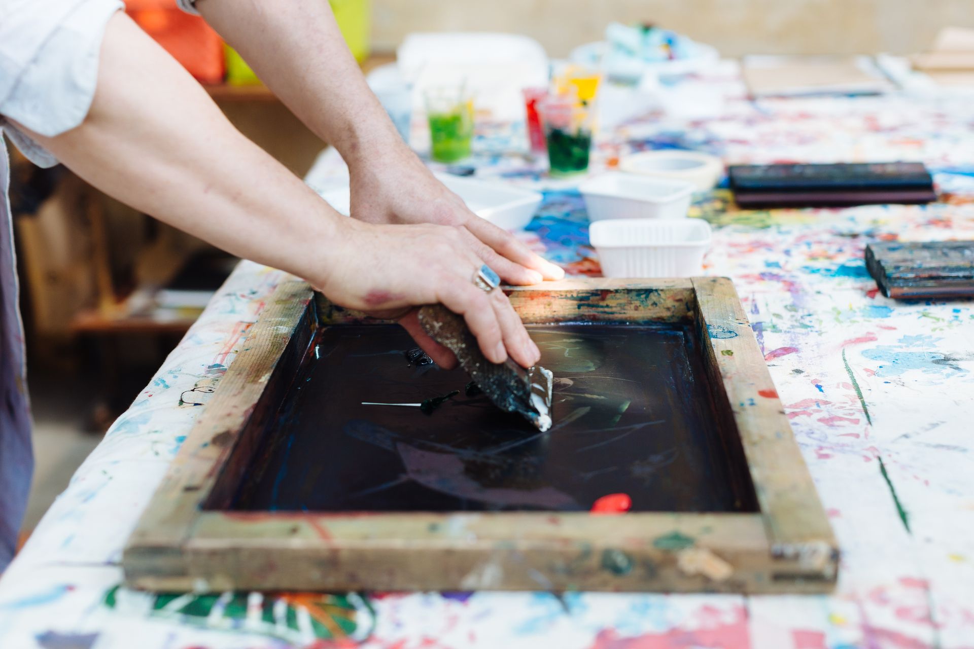 A Person Is Using a Squeegee to Remove Paint from A Screen - Jasper, IN - Impressions Printing Inc