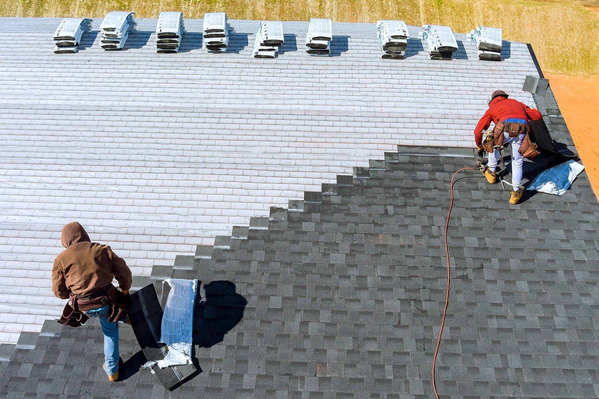 Two workers on a shingled roof, one repairing dark shingles near the ridge and one near the lower left.