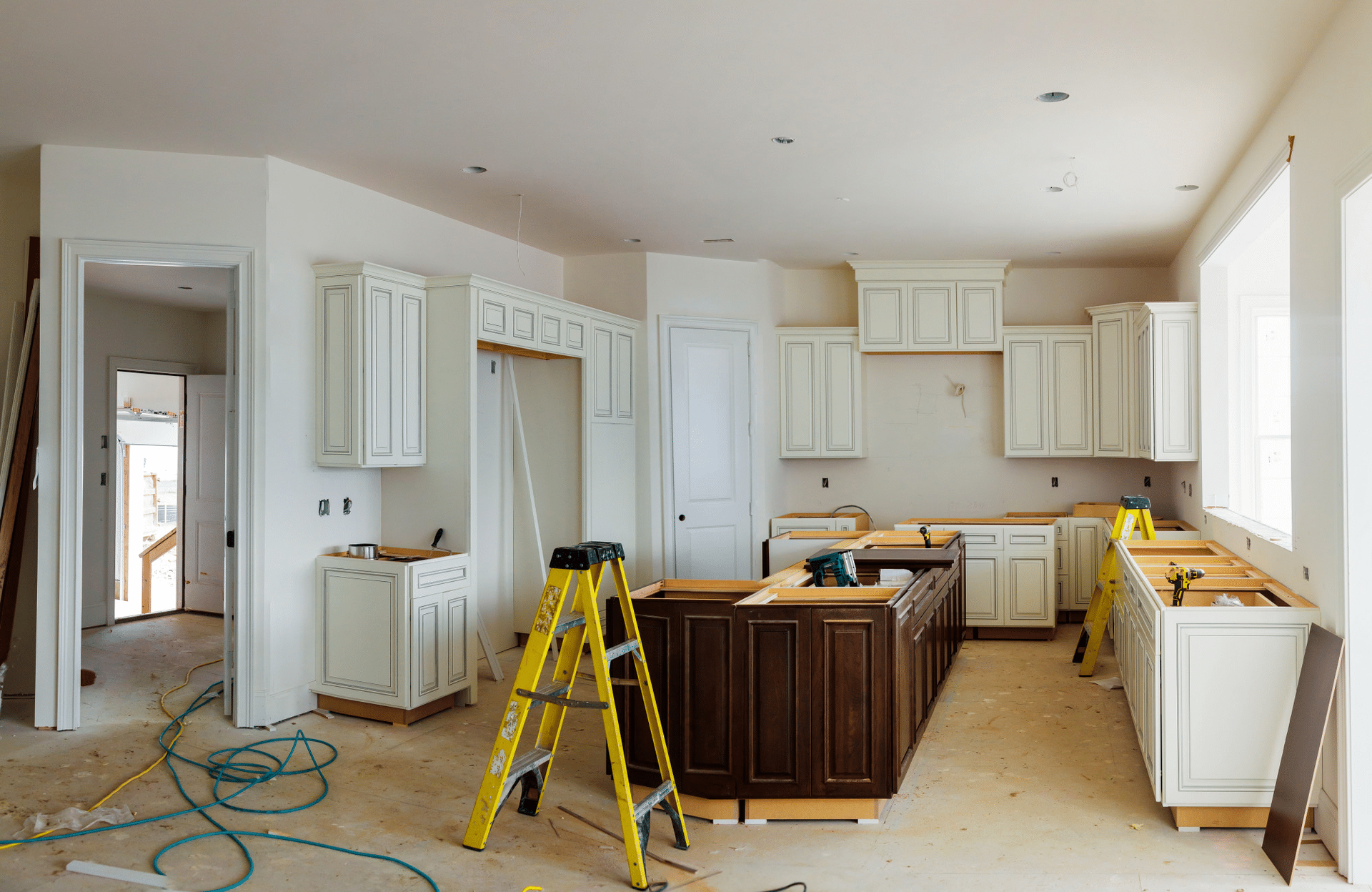 Kitchen under renovation with white cabinets, yellow ladder, and unfinished floor
