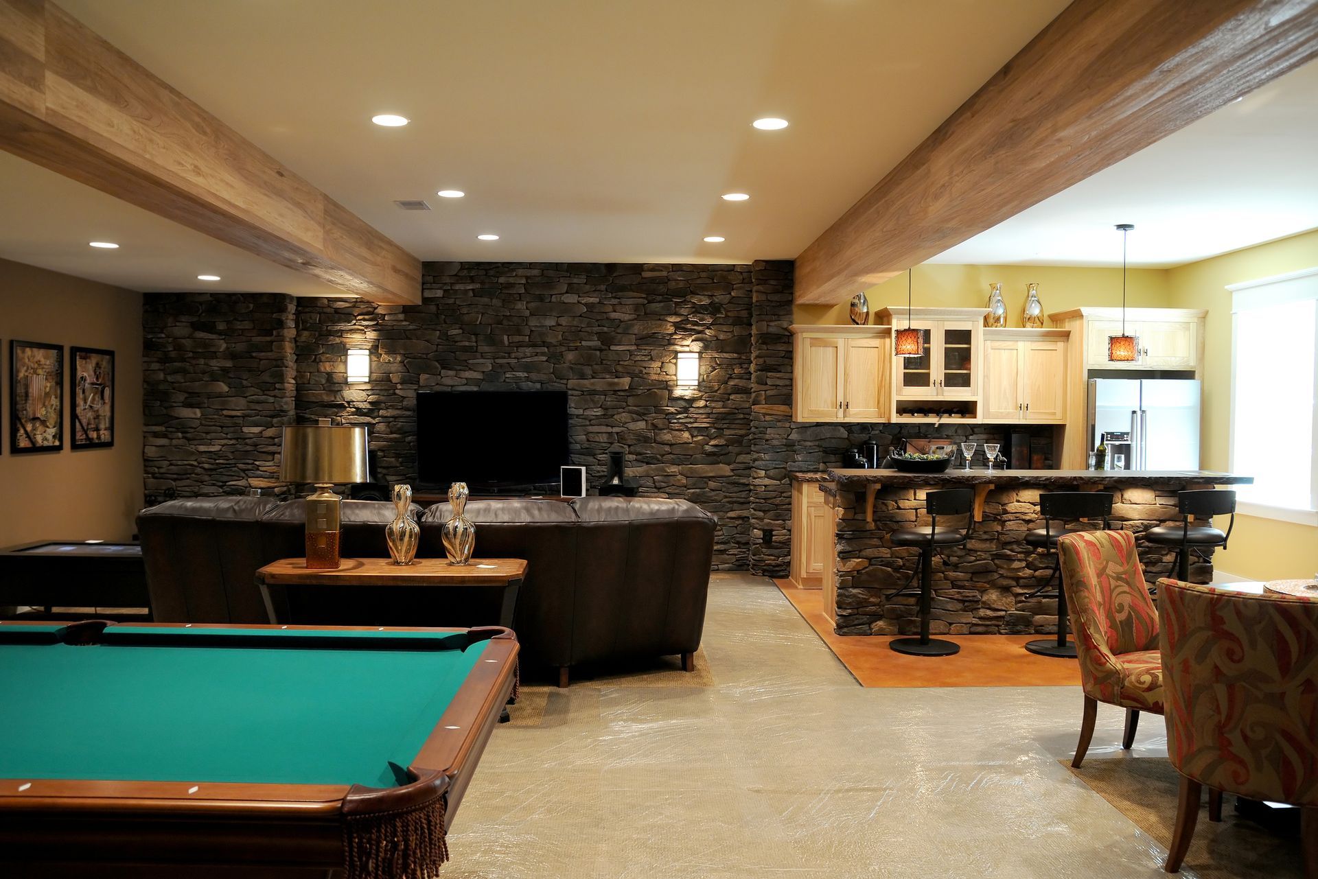 Basement game room with pool table, bar seating, dark stone wall, and TV entertainment area
