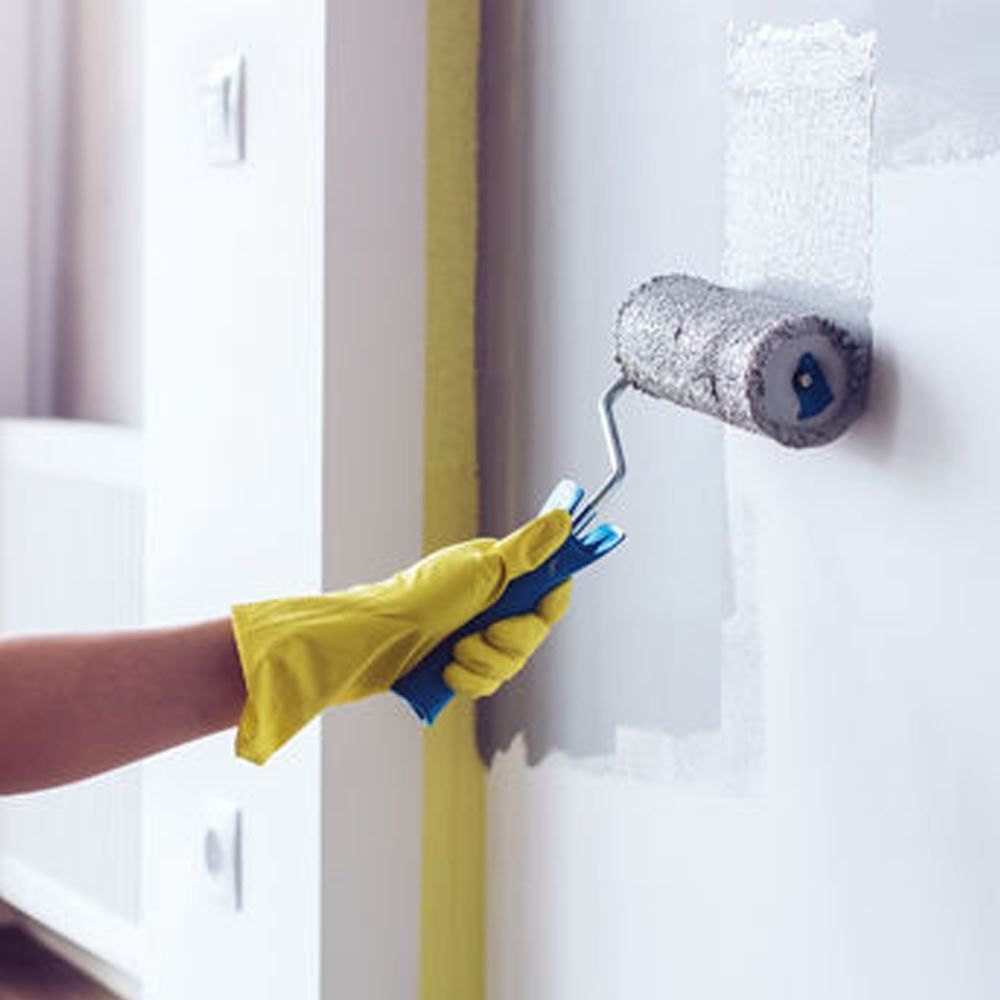 Gloved hand painting a white wall with a roller, adding fresh paint near the edge